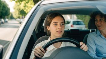 Une jeune femme au volant d'une voiture d'auto-école avec sa monitrice, illustrant l'aide permis de conduire jeune 16-25 ans.